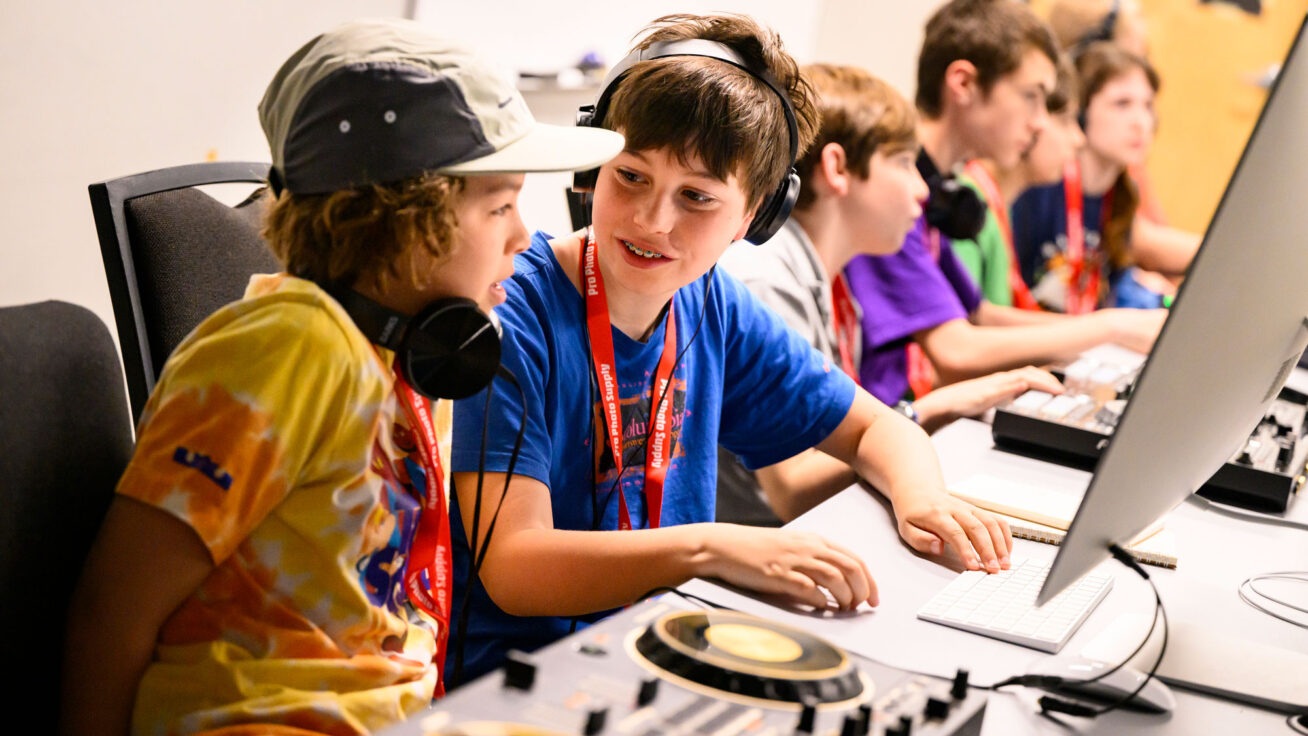 Two kids working together at a computer and DJ mixing equipment.