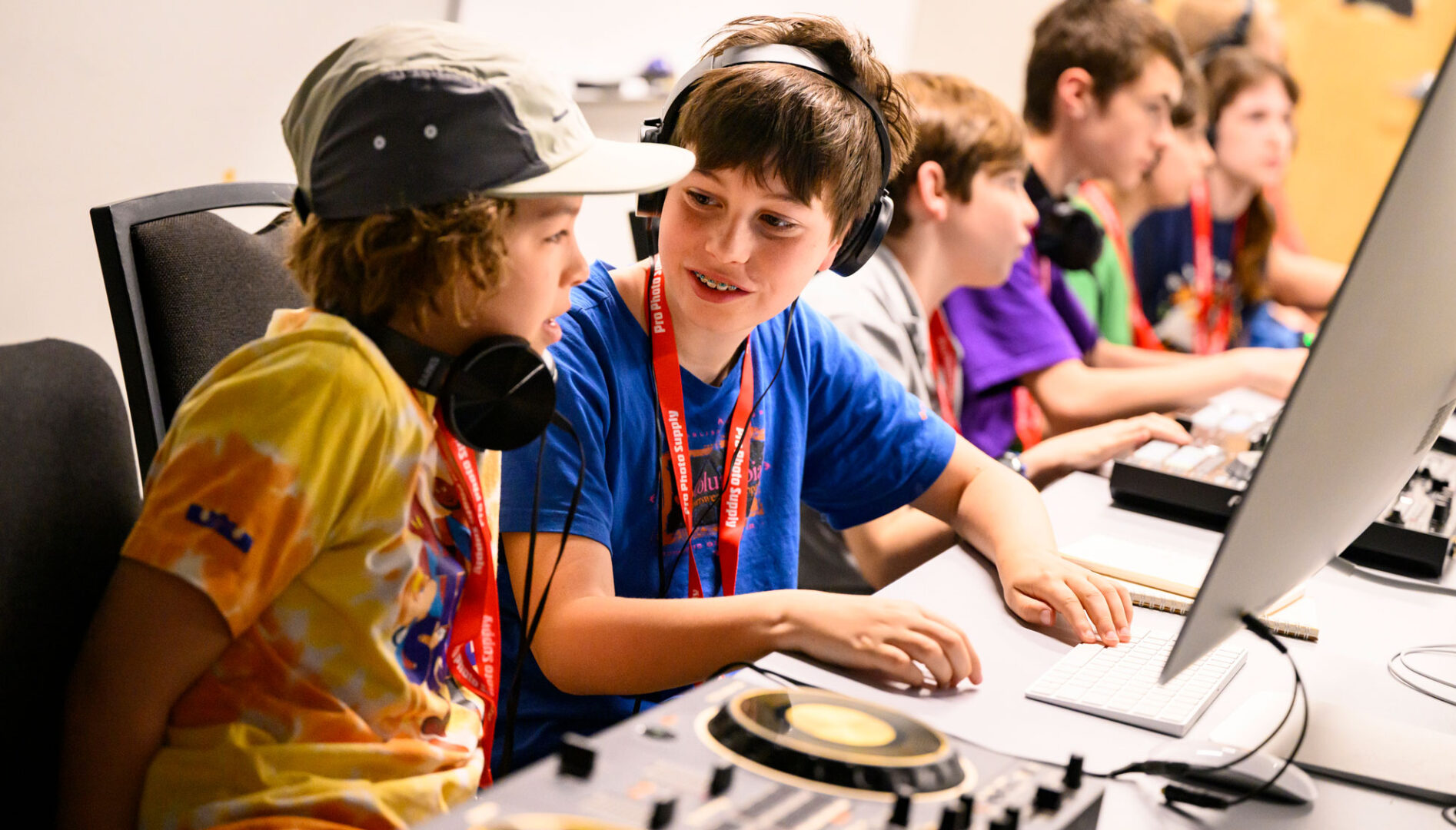 Two kids working together at a computer and DJ mixing equipment.