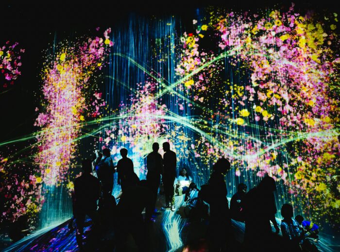 Dark scene with the outlines of people looking at multi-colored and multi-patterned lights.