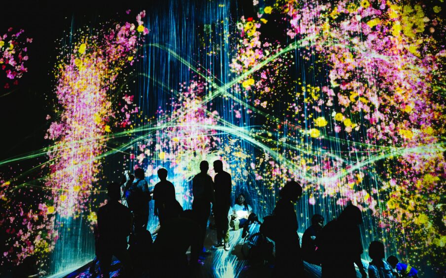 Dark scene with the outlines of people looking at multi-colored and multi-patterned lights.