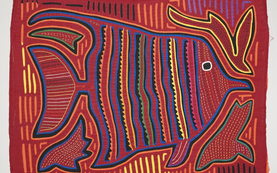 Image Description: Fish Mola. Kuna artist. Cotton. 13 ¾ in x 17 ½ in. Bright red fabric with a fish embroidered on it. The fish is outlined in a thick black line with a bright blue line against it on the inside and a bright orange line on the outside. The fish is triangular shaped and facing the right. It has a large flat tail and small fins in front. Its mouth is small and beak shaped. It has a large black eye with a white outline. Its face is a series of lines of small dots that are yellow and red. Behind the eye, solid colorful lines: blue, black, pink, red, pink, scalloped black, blue, red, blue, black, yellow, red, yellow, scalloped black, blue, red, blue, black, orange, red, orange, scalloped black, blue, red, blue, black, green, red, green, scalloped black, blue, red, blue, black, yellow, red, yellow, scalloped black, blue, red, blue, black, orange, red, orange, scalloped black, blue. The tail has several horizontal lines of varying colors (green, yellow, white, red, orange). There are also lines of various colors between the outline of the fish and the edge of the fabric (black, yellow, orange, and purple). There are four shapes at the corners of the fish. The top left is a triangular shape with a green and black outline and yellow dots. The top right is a shape that resembles a bird with a long tail diving downward. It is outlined in yellow and black and has dark spots. The bottom right also resembles a bird diving and is outlined in green and black with yellow spots inside. The bottom left is flame shaped with blue and black outlines and yellow dots inside.