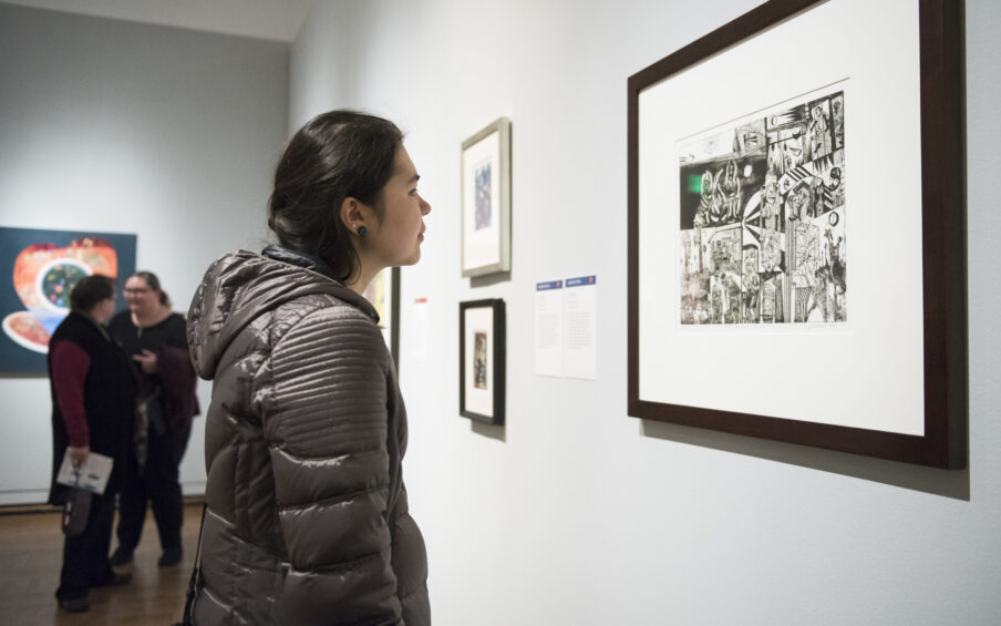 Photo of a person wearing a winter coat looking intently at a painting.