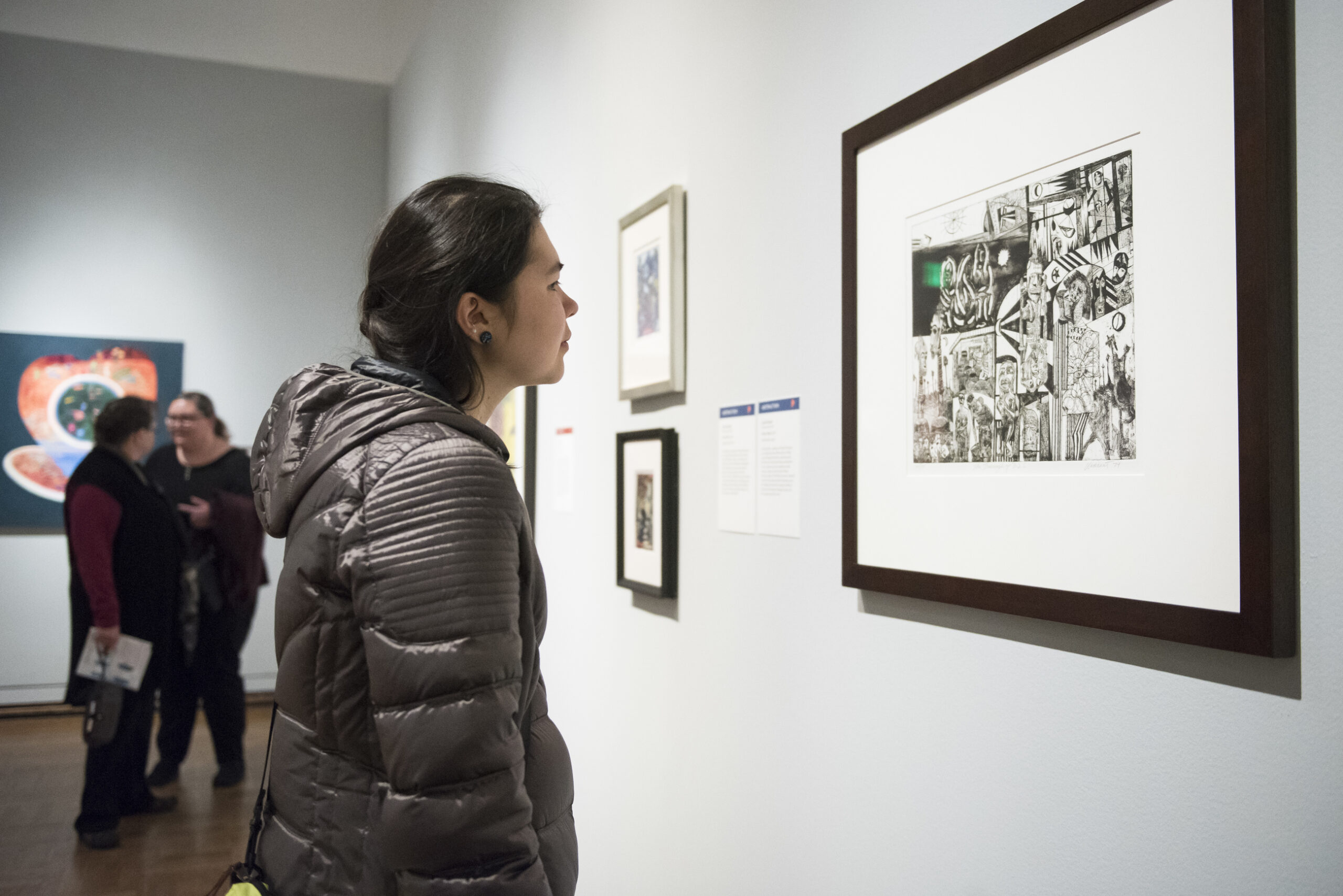 Photo of a person wearing a winter coat looking intently at a painting.