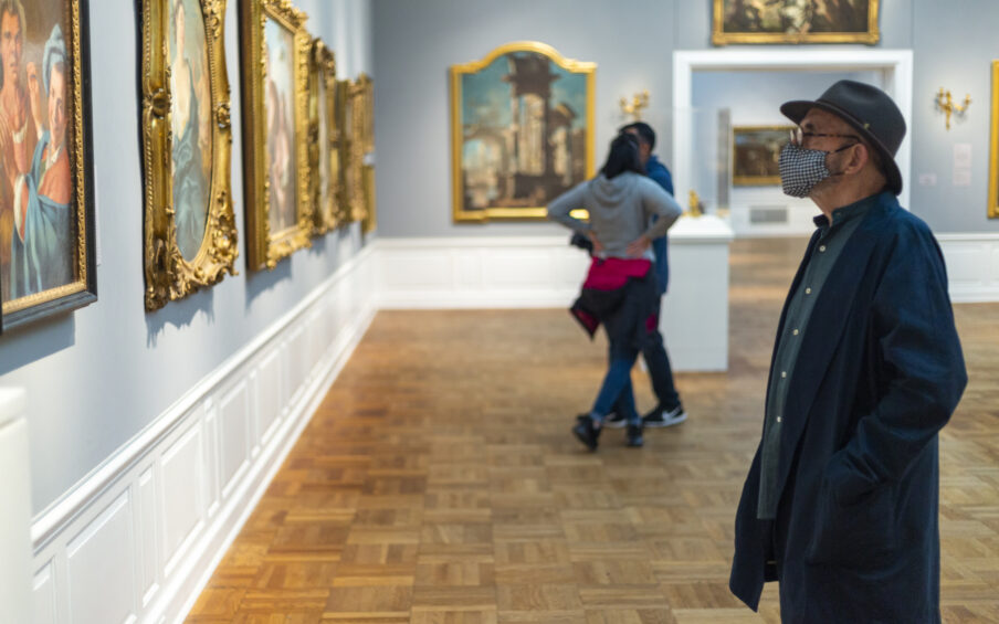 Man in a black hat and a face mask looking at a painting