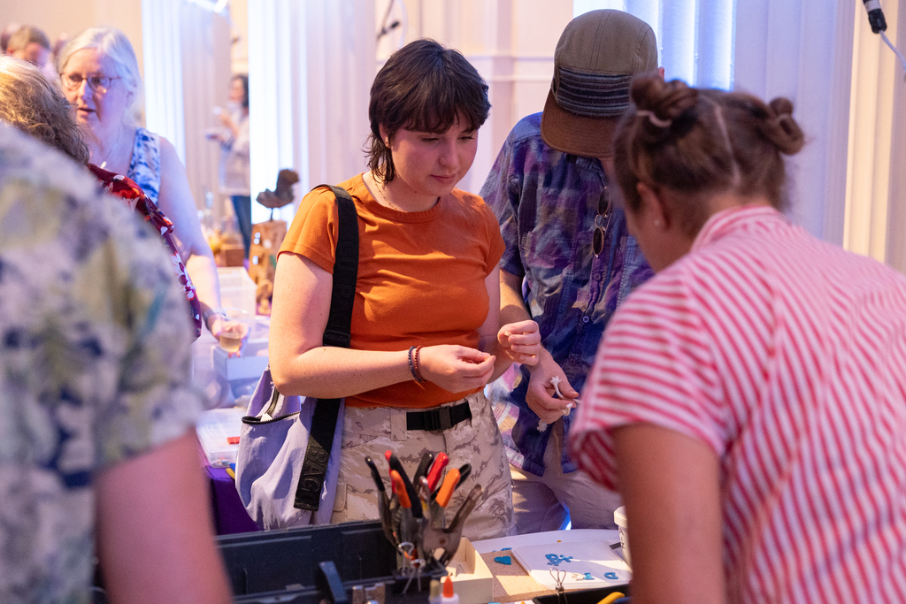 An individual is in front a of table in a crowded room, working on a toy-making activity. 