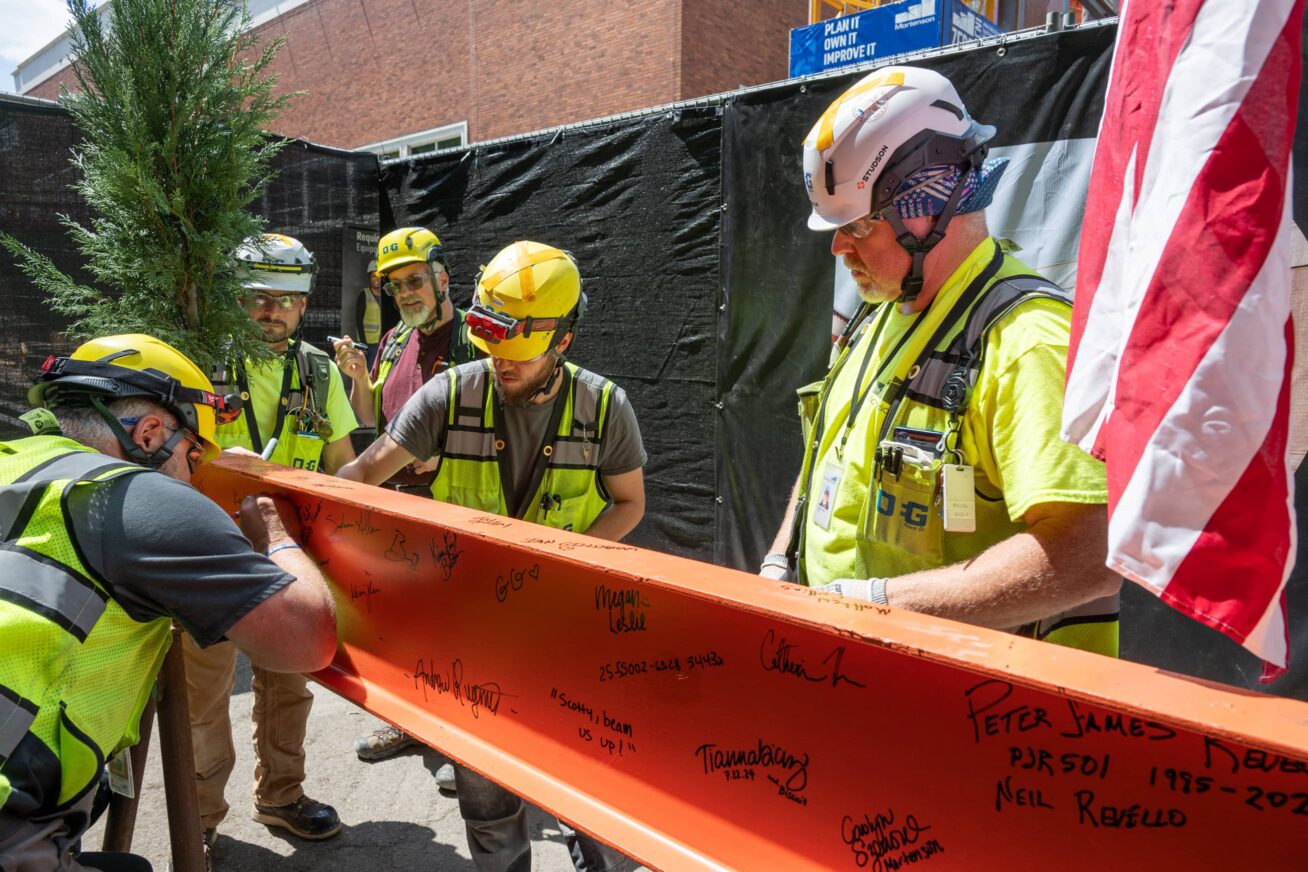 Construction workers signing an orange steel beam