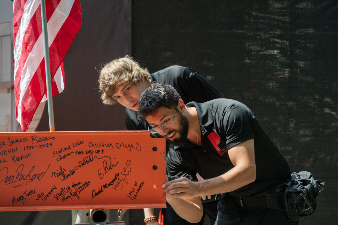 Two Museum staff members signing an orange steel beam
