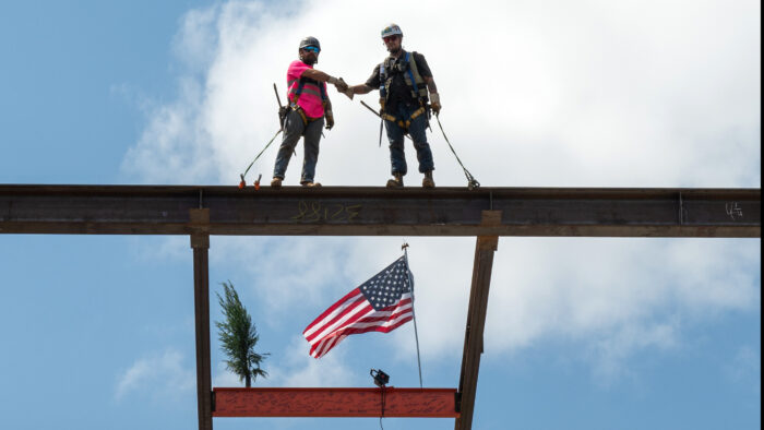 Two construction workers on top of a steel beam shaking hands