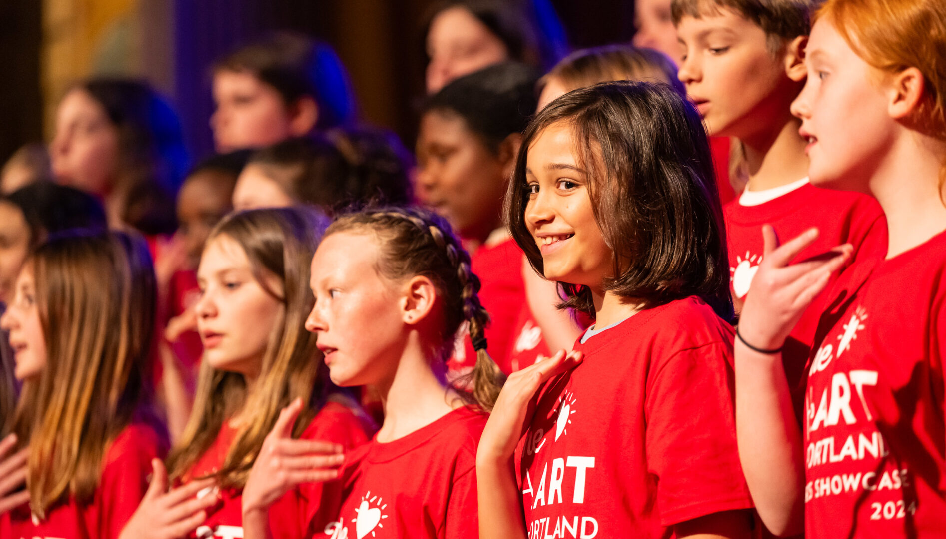 Photo of a group of kids in red HeART of Portland t-shirts on stage