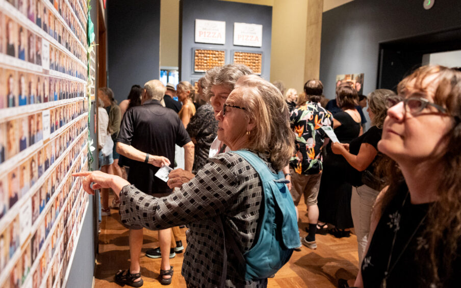 A large group of people examining art in a gallery.