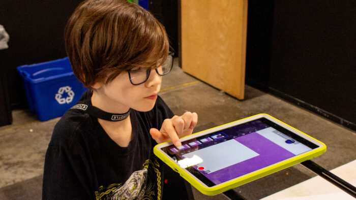 A child with short hair and eyeglasses making art on an iPad.