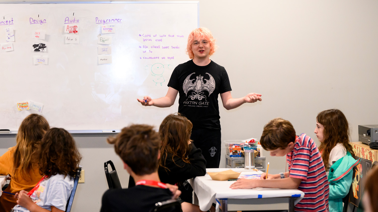 Photo of a teacher with pink hair in front of a classroom of seated middle-grade students
