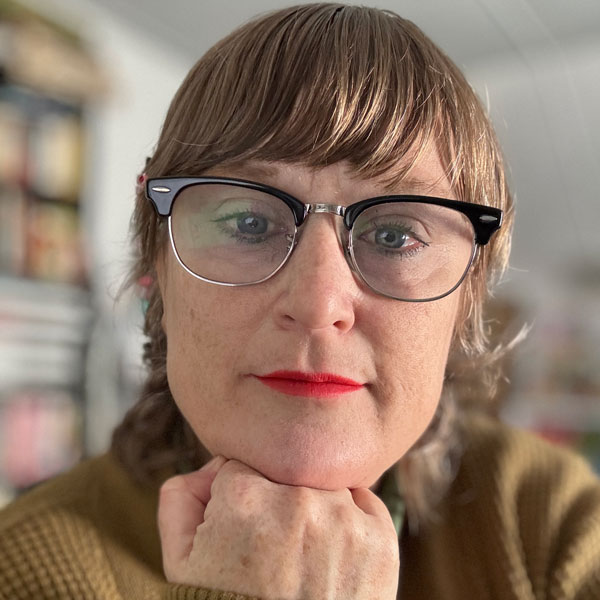 Photo of a woman with red hair and eyeglasses resting her head on her fist.