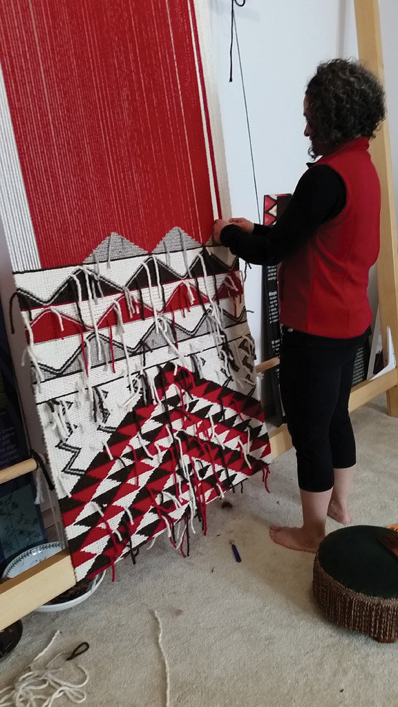 Photograph of a woman standing in front of a loom