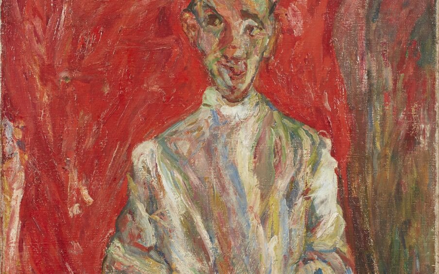 A vertical painting featuring a full-length male figure standing with his hands clasped in front. His left foot is placed in front of the other pointing to the right of the picture. He wears a cap atop a long face with a pointed chin. His ears protrude from either side of his head, bits of black hair poking out by his ears and at his forehead. Large dark eyes look off to the viewer’s left. He wears what appears to be a long-sleeve, high-collared white shirt. When examined more closely, the white shirt as well as his cap and shoes are made up of many colors in addition to white—grays, blues, green, yellows, tan, orange, and dashes of red applied in broad, rough brushstrokes. Similarly, his baggy, brownish pants are painted with strokes of brown, black, yellow, red, orange, and tan. To the left of the figure stands a brown chair with ornate slatted back. Behind the figure is a field of mottled red tones making up most of the width of the painting, suggesting a curtain. A narrow swath of reds, browns, yellows complete the right side of the painting running from top to bottom.