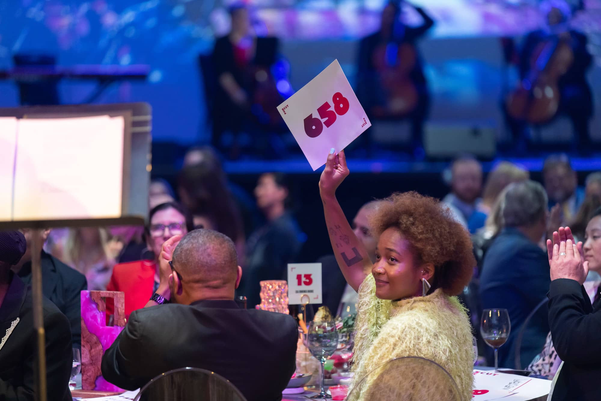 People sitting at tables. One person is holding up an auction card.