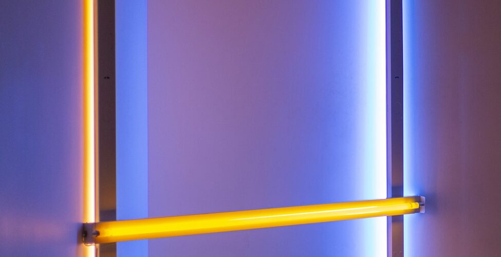 Image description: Untitled (to Donna) 2, 96 ¼ x 96, fluorescent light. An installation of fluorescent lights positioned in a corner consisting of two bright yellow lights running horizontally at floor and knee level and two fluorescent lights running horizontally at each end with the light component facing the wall. The horizontal lights are bright blue at the right and mauve at the left. All four lights cast their colors on the corner walls and floor.