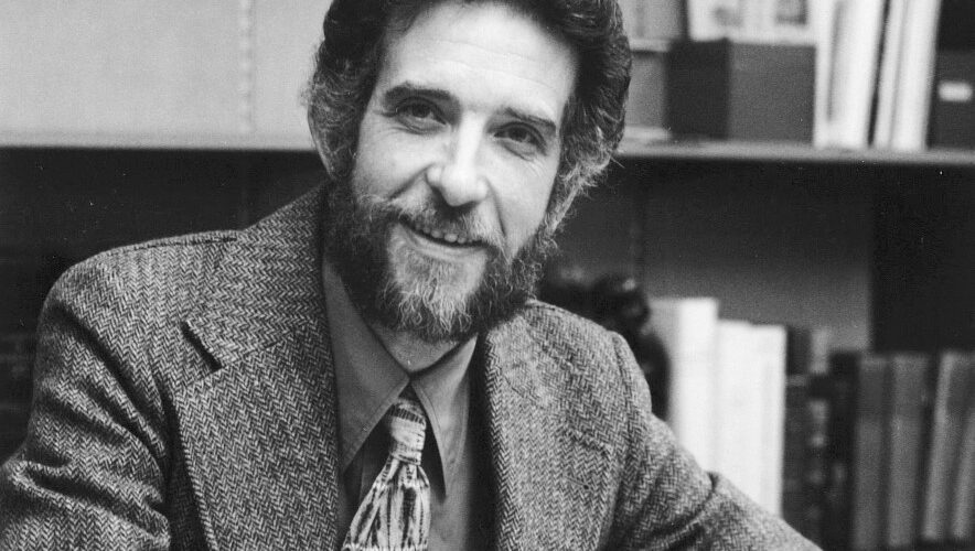 Black and white photo of a man with a beard wearing a suit and tie.