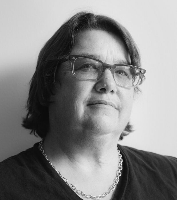 Black and white portrait of a women with shoulder length hair, wearing eyeglasses, a v-neck blouse and a necklace