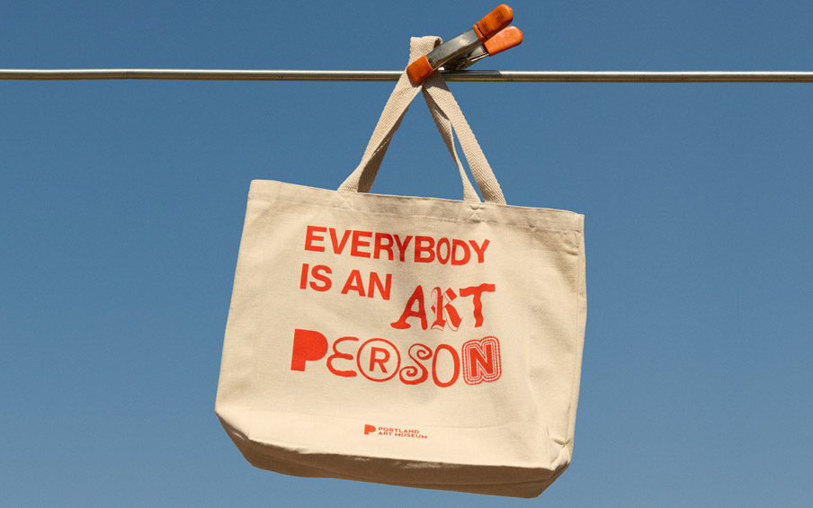A tote bag with the text Everybody is an Art Person hanging from a pole.