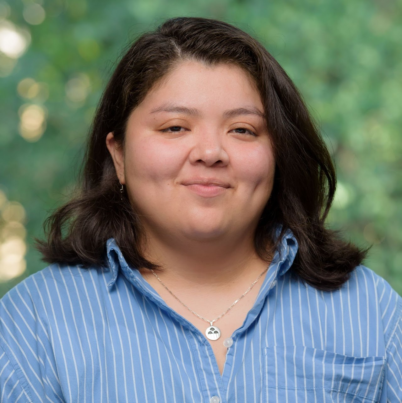 Portrait of a smiling woman with long brown hair, a blue and white striped shirt, and a silver necklace