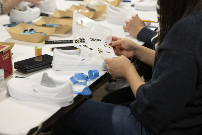 Photo of someone's hands working on decorating a white sneaker, surround by art materials