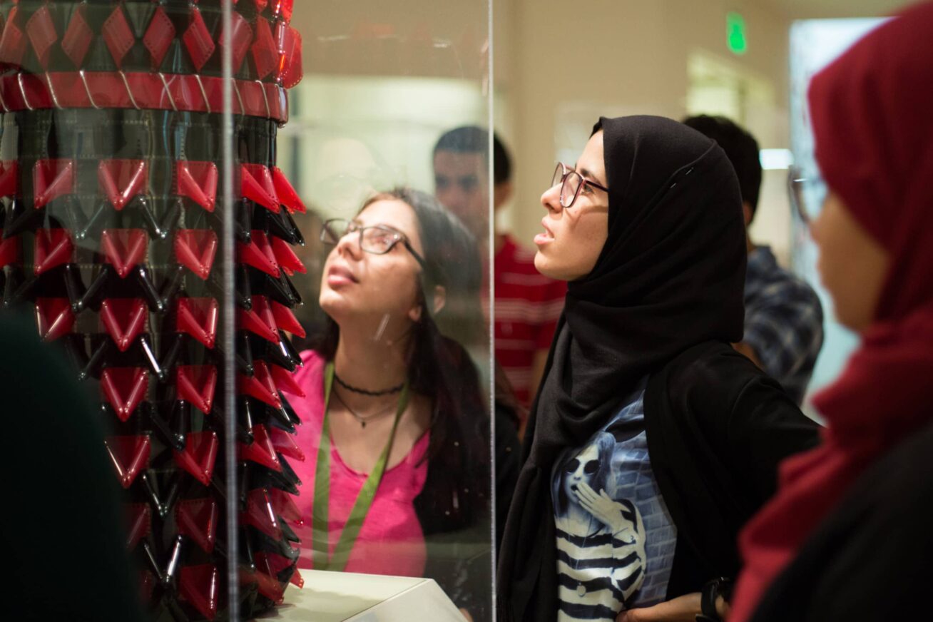 A small group of people examining a sculpture placed behind a glass case.
