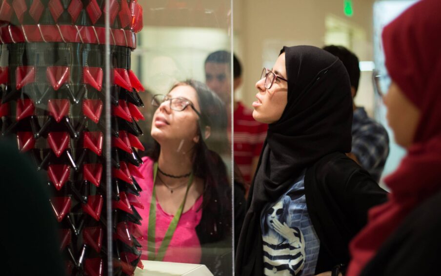 A small group of people examining a sculpture placed behind a glass case.