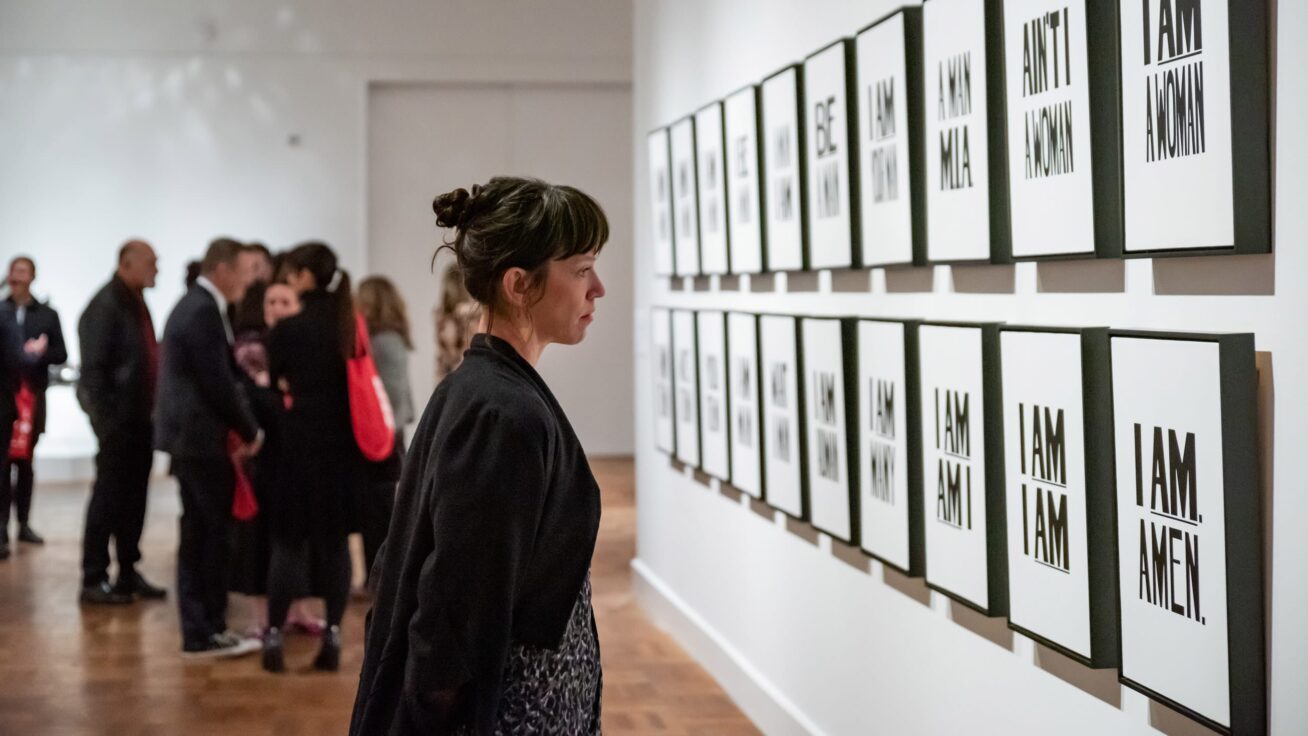 Several people viewing multiple pieces of framed artwork on a gallery wall.