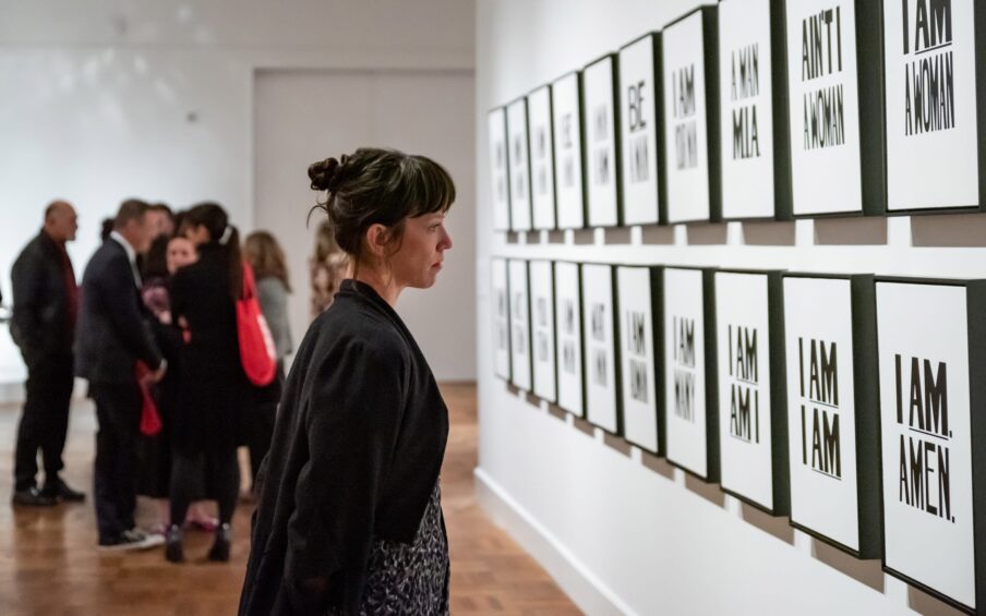 Several people viewing multiple pieces of framed artwork on a gallery wall.