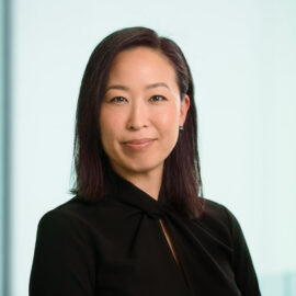 Color photograph of a woman with long, brown hair smiling and wearing a black, collared shirt