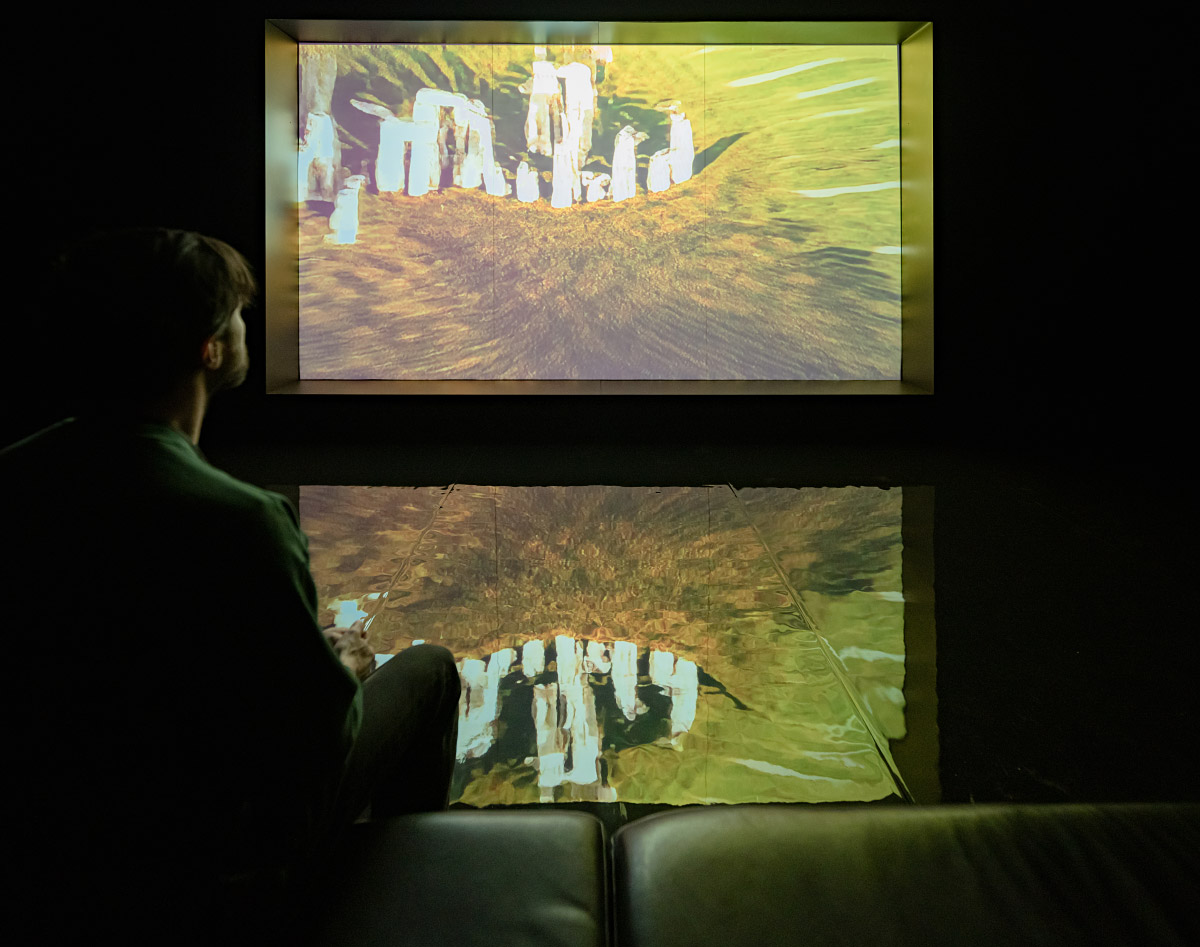 Dark room with a video screen projecting stonehenge on a psychedelic yellow and orange background.