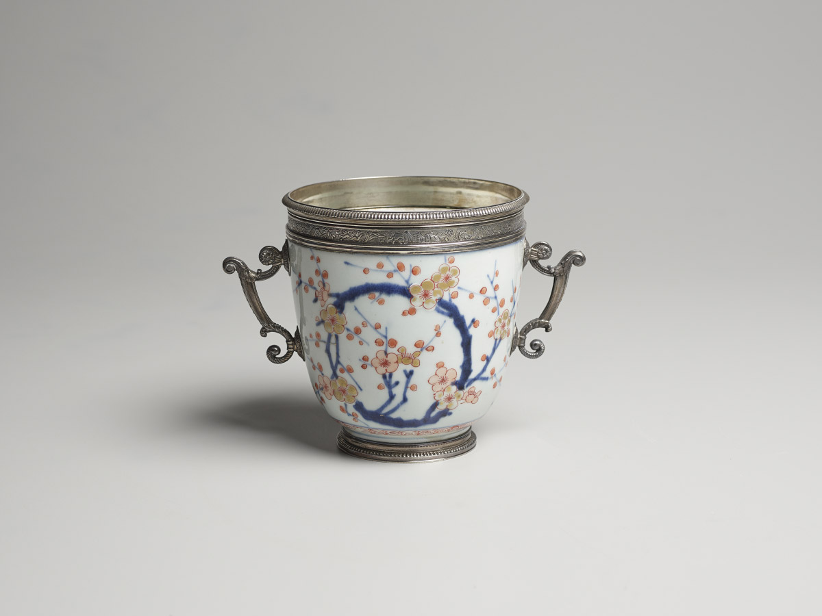 A small porcelain bowl decorated with cherry blossoms, with silver handles on both sides and a silver rim