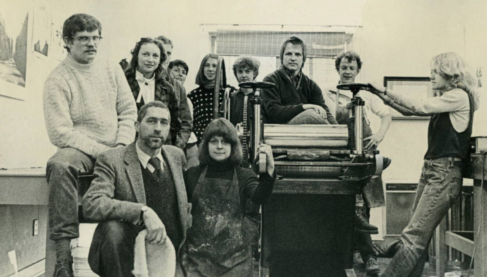 A group of people sitting and standing around printing equipment.
