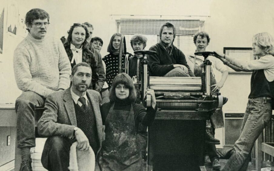 A group of people sitting and standing around printing equipment.