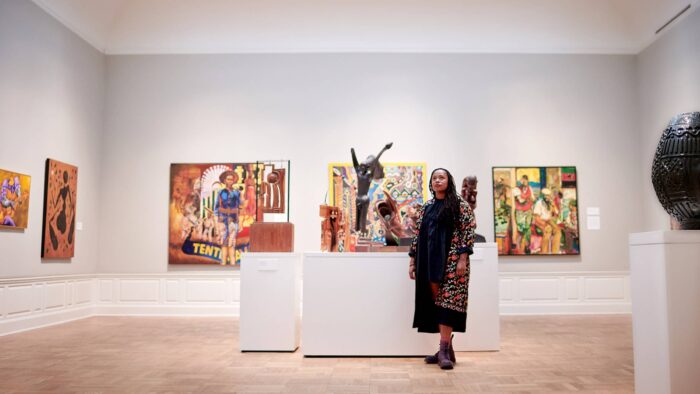 Person standing in gallery space surrounded by paintings and sculptures.