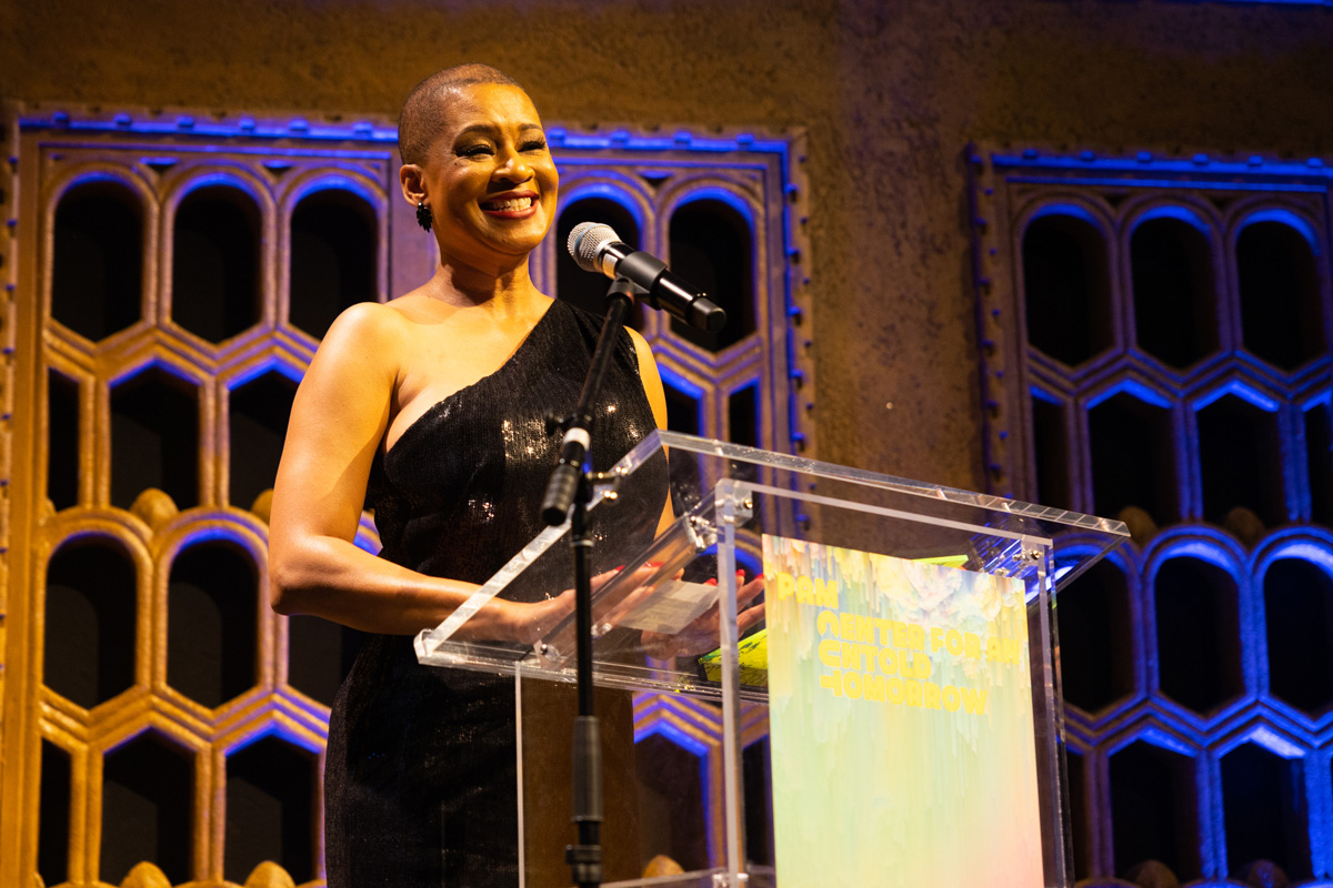 Smiling Black Woman in a one-sleeved dress at a podium on stage