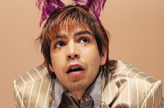 Julio Torres wearing pink fuzzy ears on his head and a gold and white striped shiny suit.