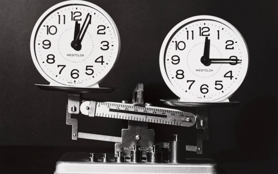 Two analog clocks sitting atop a balancing scale.