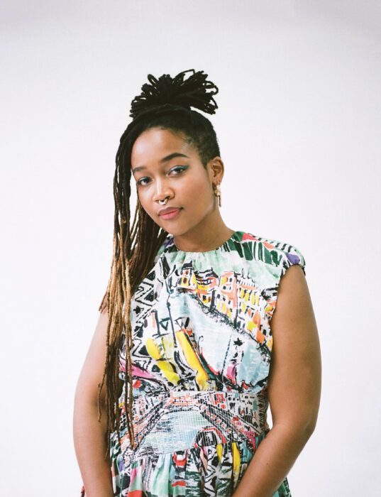 Portrait of a Black woman with long braids, a septum ring, gold earrings and a colorful, sleeveless dress