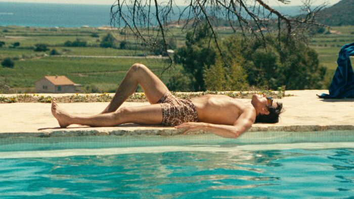 A man in a bathing suit laying at the edge of a pool.