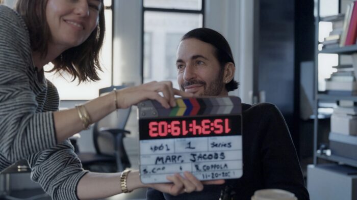 Sofia Coppola leaning in with a clapboard in front of Marc Jacobs who is looking lovingly at her.