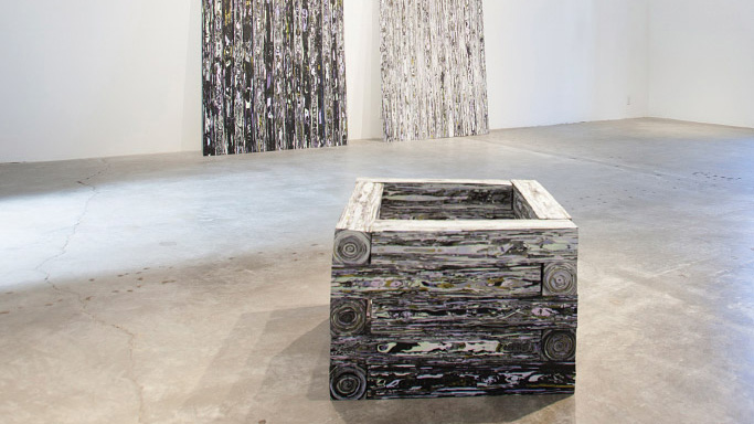 Photo of a gallery with a concrete floor, a silver metallic-looking box in the middle, and two groups of shiny streamers hanging on the white wall