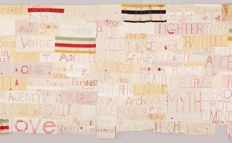 Image description: Companion Species: Ferocious Mother and Canis Familiaris. Marie Watt. 2017. Reclaimed wool blankets, embroidery floss, and thread. 108 in x 217 in. A long rectangular work composed of numerous other horizontally oriented rectangles. Each rectangle contains a word embroidered in red thread on various shades of cream to pale tan cloth in assorted stitches and styles. Some of the largest words are Ancestor, Myth, Love, Voice, Fighter, Custodian, Gratitude. Smaller words include Seeker, Care, Watcher, Legacy, Healer, Advocate, Interpreter, Wild, and Catalyst. Interspersed among the words are rectangles made of striped blankets in red, green, yellow, and black.