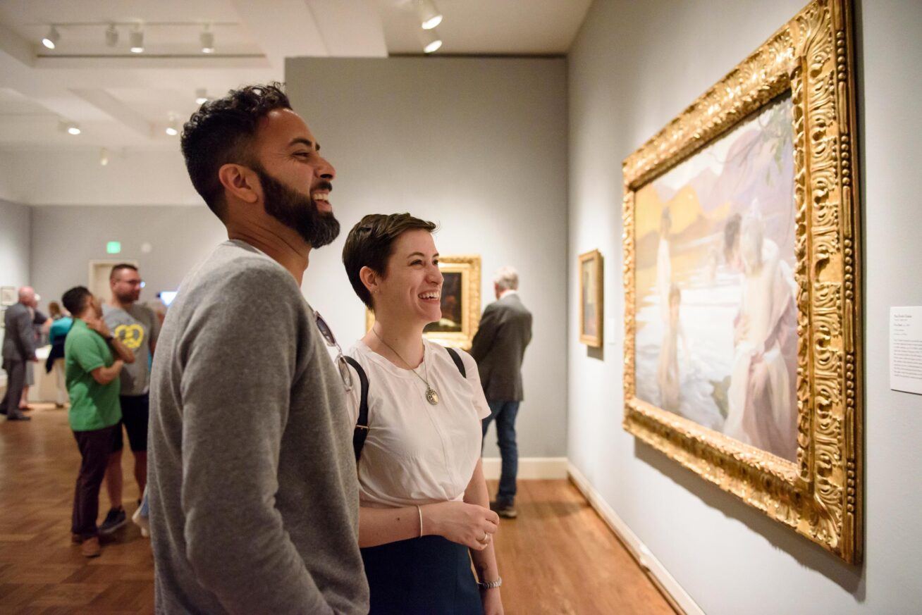 Two people viewing a framed painting in a gallery.