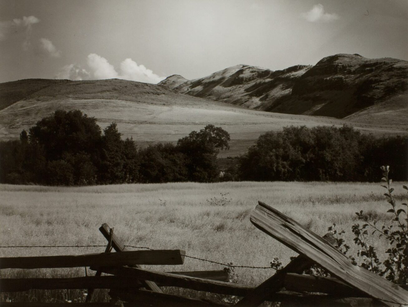 Black and white photograph of open hills with a broken fence in the foreground.