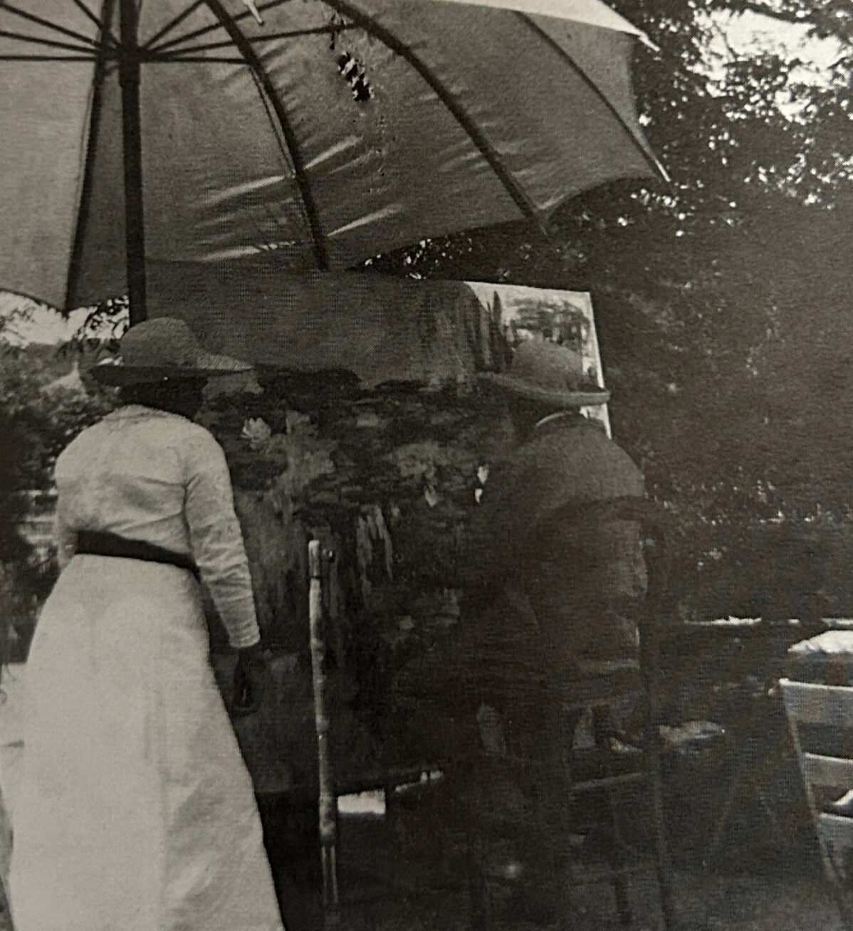 A person sitting at an easel outdoors, painting waterlillies. Another person stands at their side.