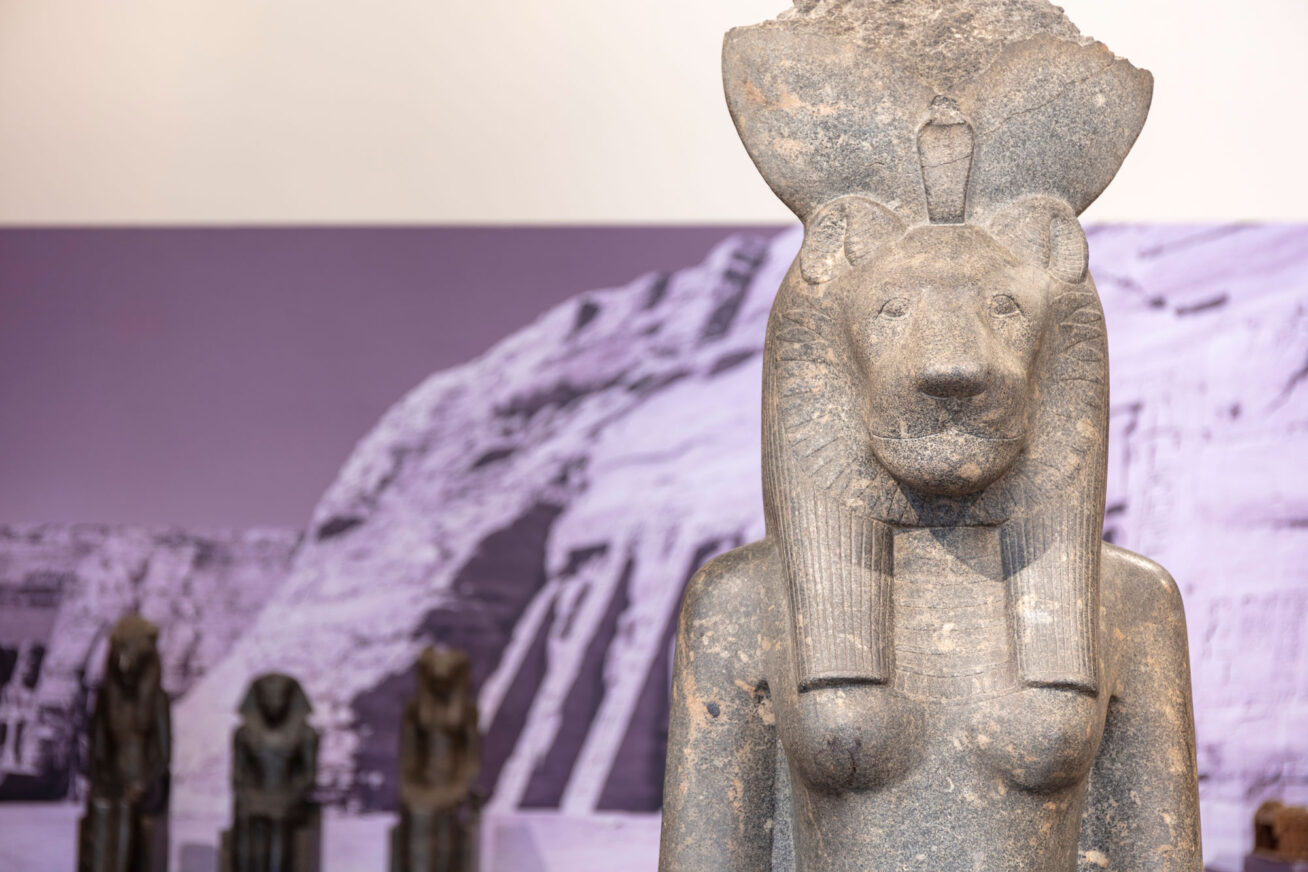 Statue of an Egyptian god with an image of the pyramids on the wall behind