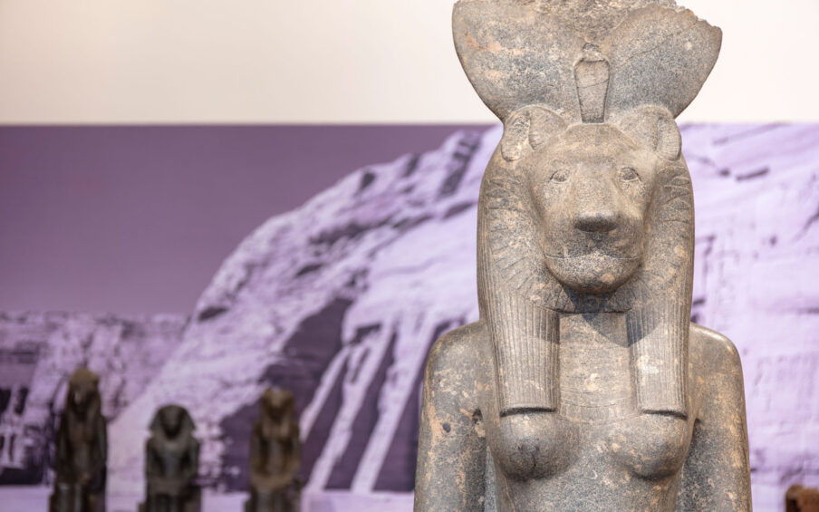 Statue of an Egyptian god with an image of the pyramids on the wall behind