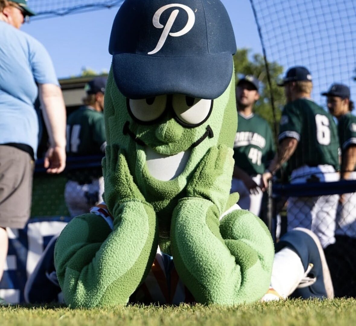 Photo of the Portland Pickles baseball team mascot, Dillon T Pickles, in a green pickle costume and a blue baseball hat with a P on it.
